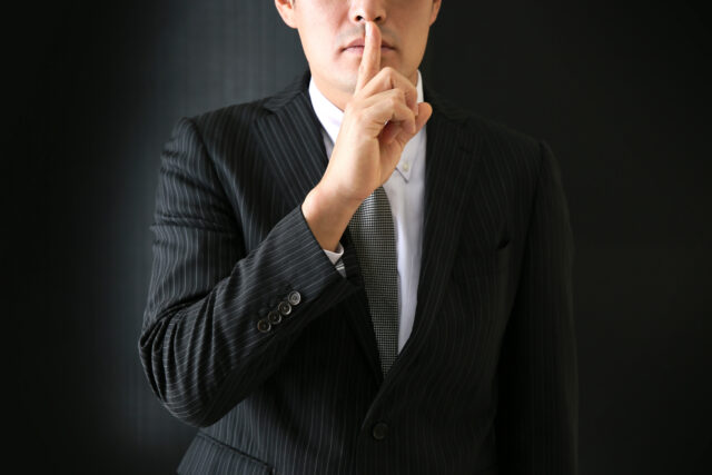 man in black suit shhh finger to lip
