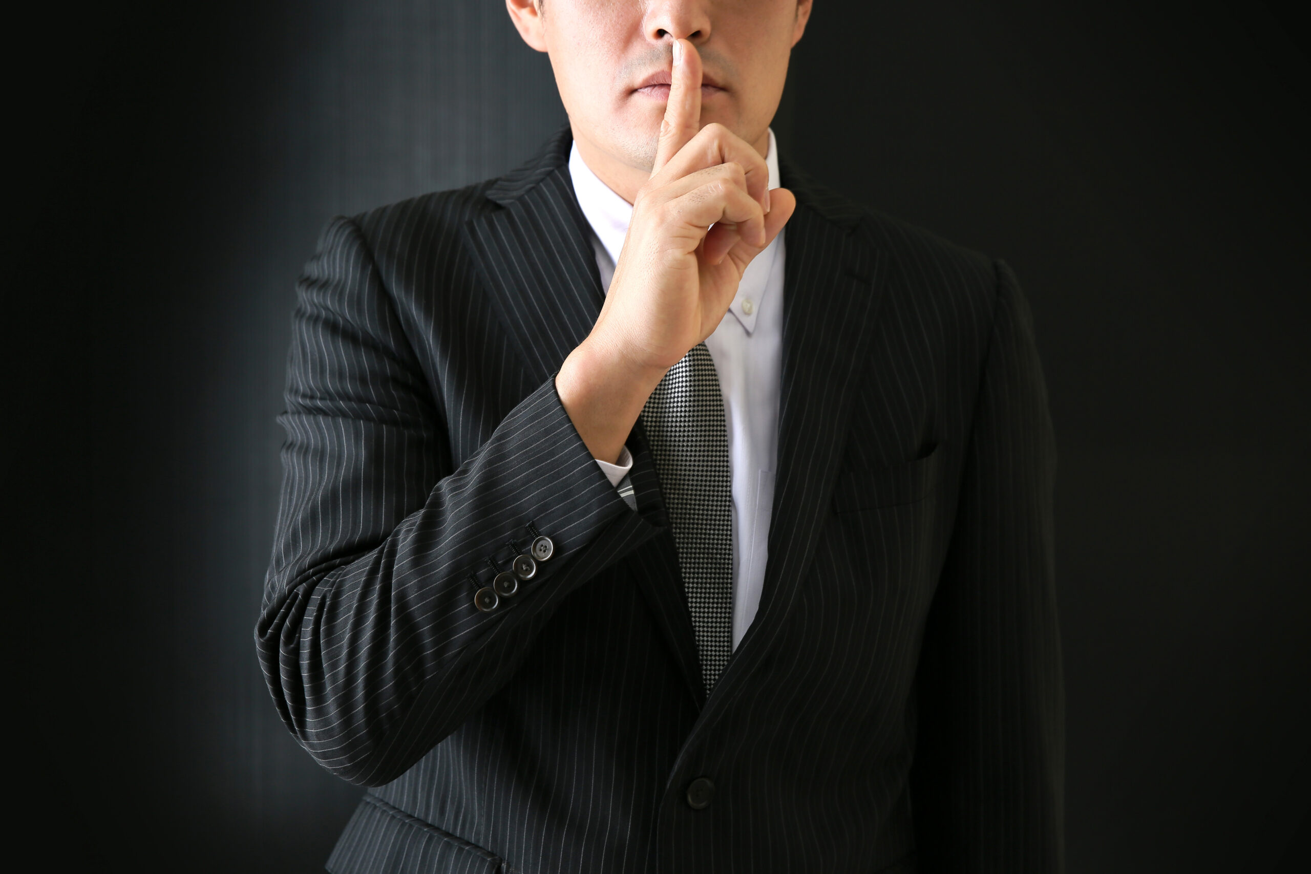 man in black suit shhh finger to lip