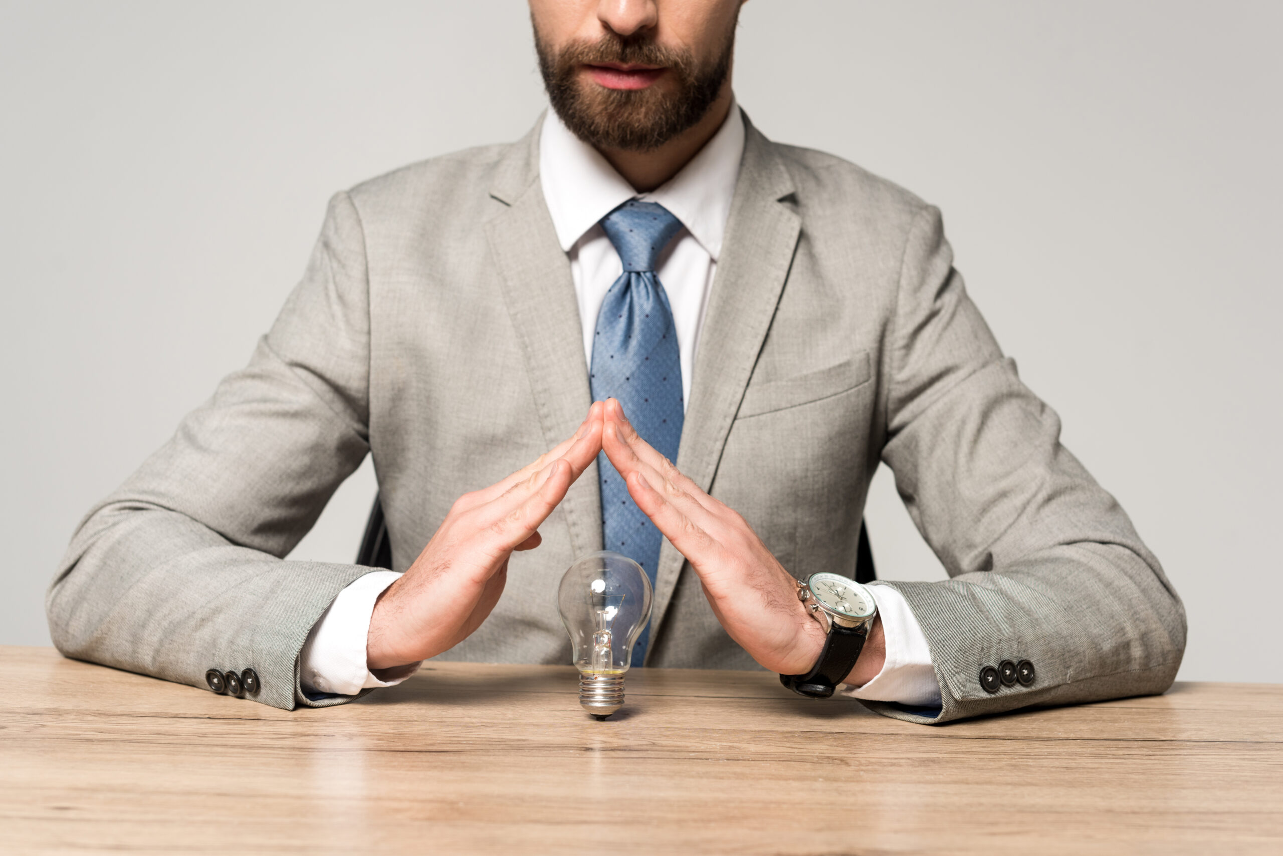 partial view of businessman showing protection gesture above light bulb isolated on grey