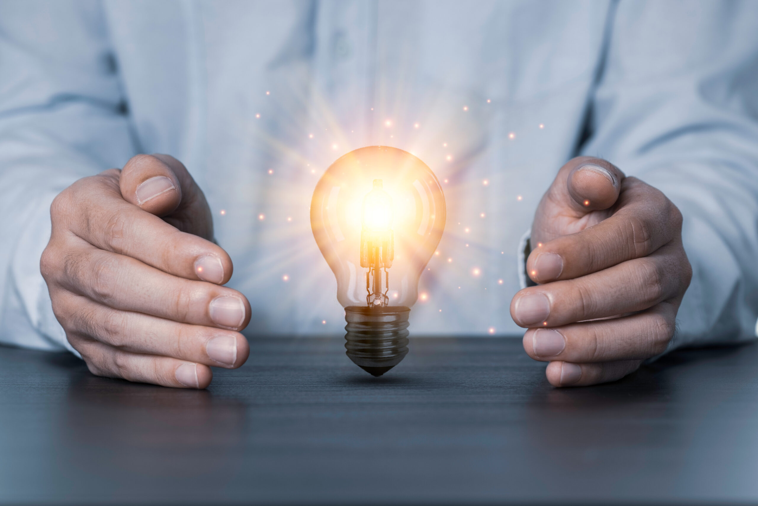 Two hands protecting the light bulb that is illuminating