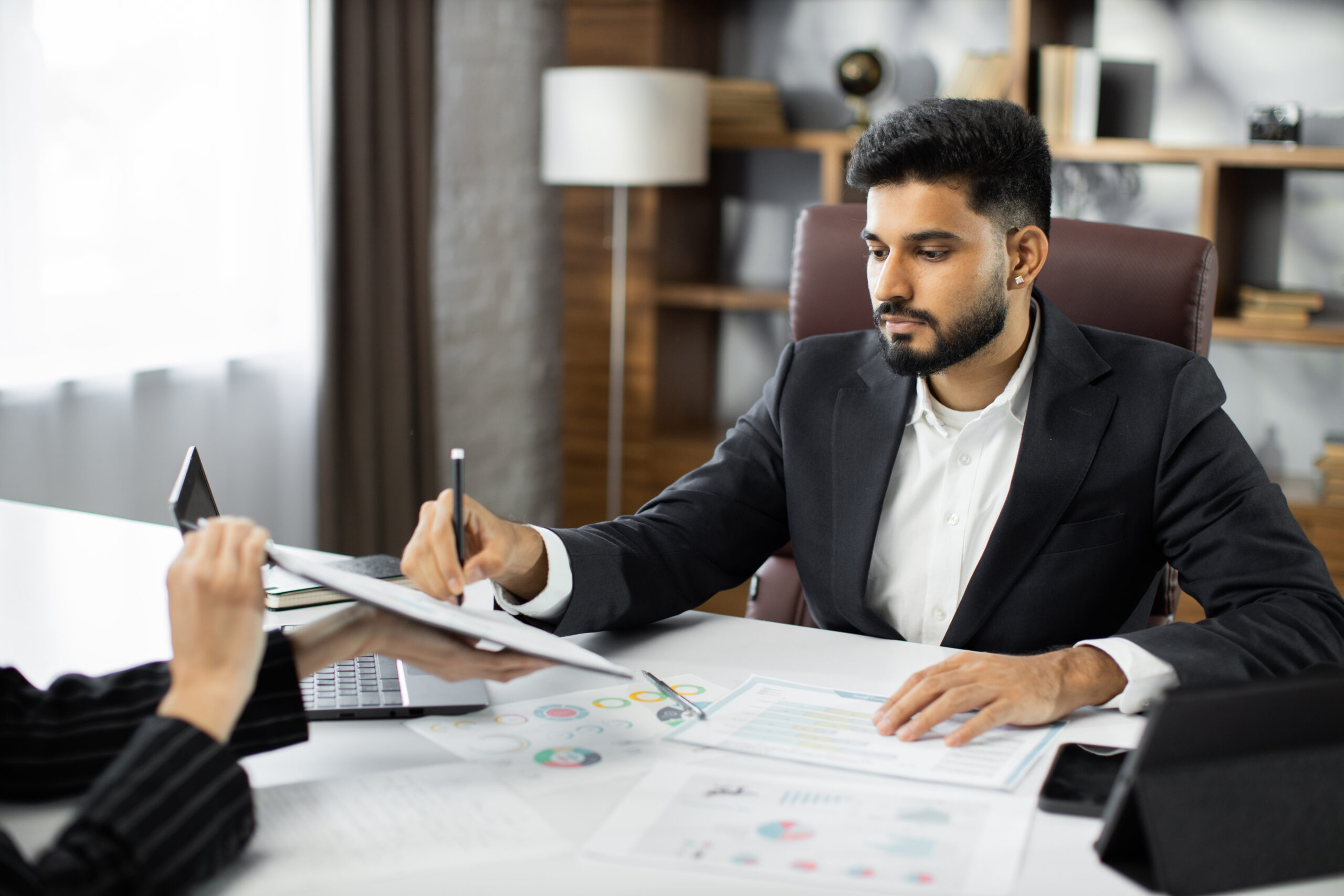 Focused young businessman signing agreement with skilled female lawyer. Concentrated financial advisor showing place for signature on paper contract document to male client at meeting in office.